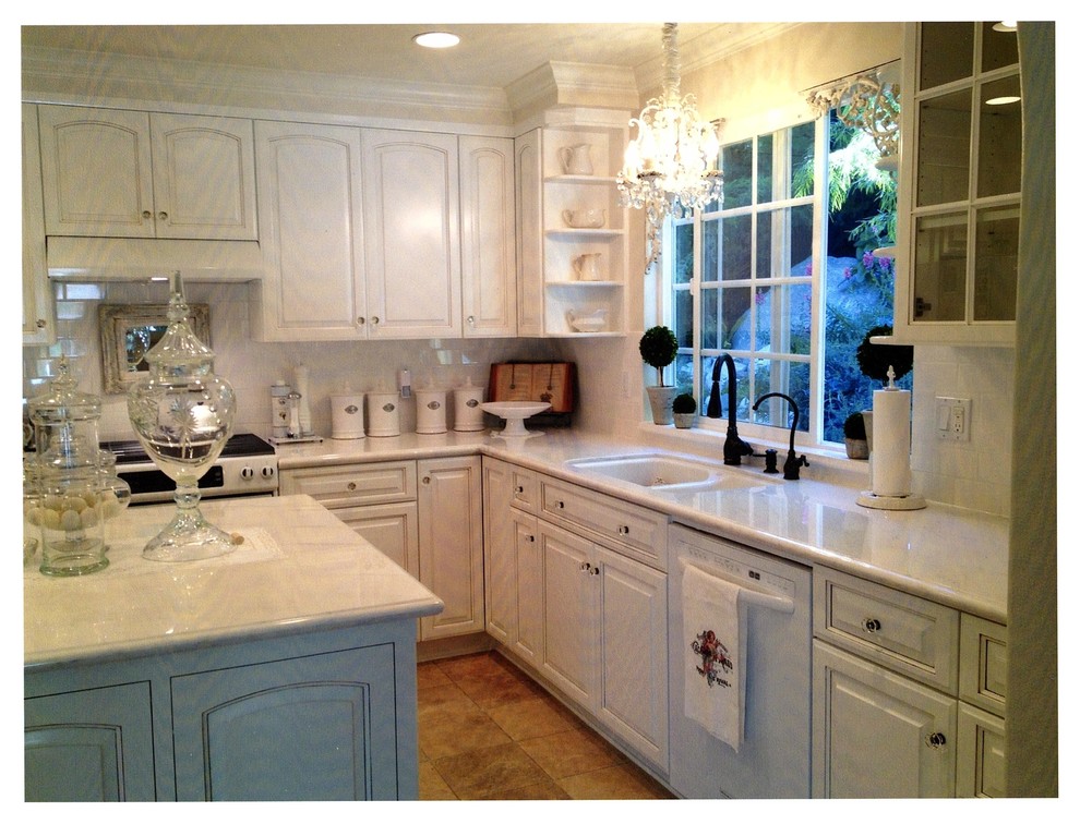This is an example of a large contemporary kitchen in Los Angeles with a double-bowl sink, raised-panel cabinets, white cabinets, white splashback, metro tiled splashback, white appliances and an island.