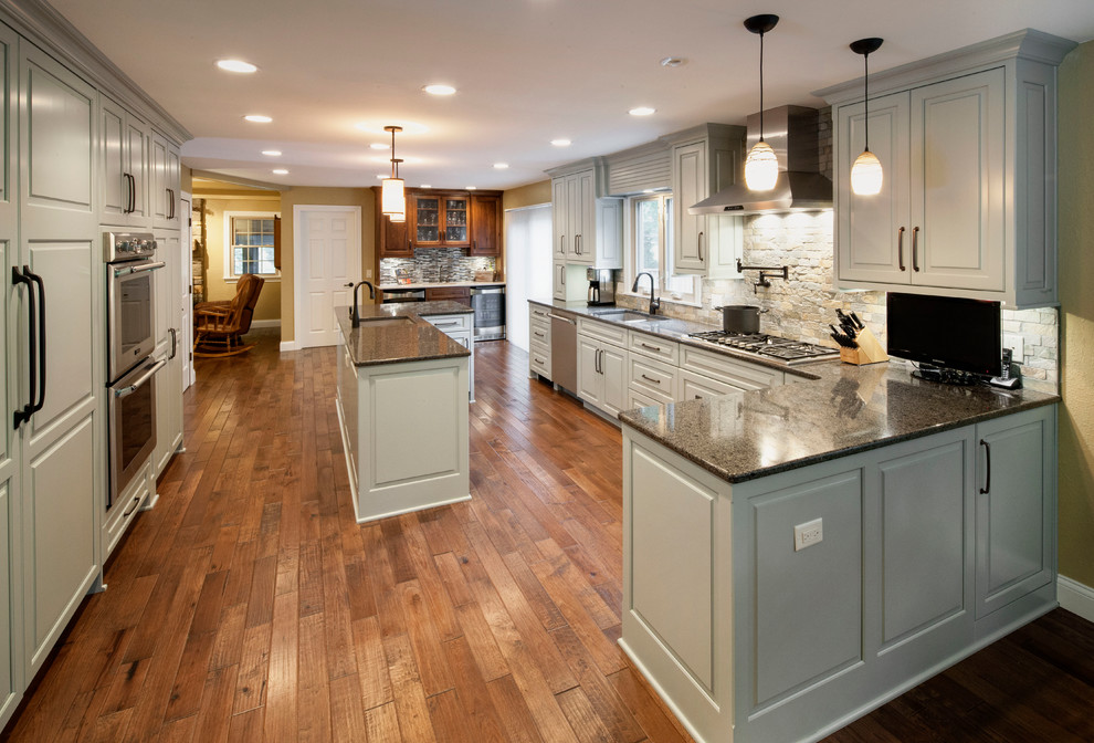 Open concept kitchen - large traditional u-shaped medium tone wood floor open concept kitchen idea in Other with a double-bowl sink, white cabinets, granite countertops, beige backsplash, stainless steel appliances and an island