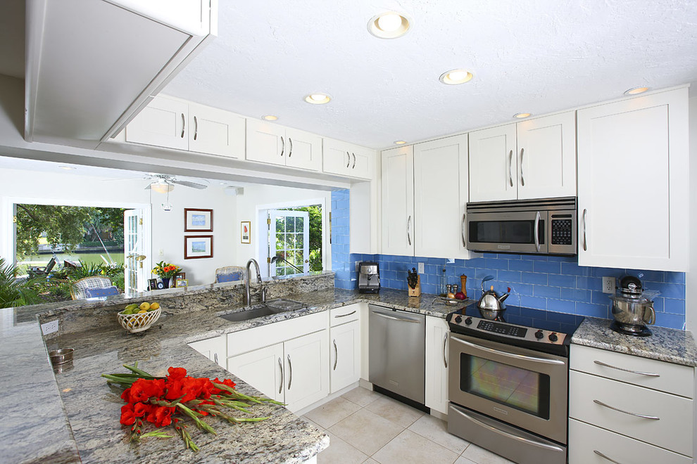 Mid-sized trendy l-shaped limestone floor and beige floor eat-in kitchen photo in Tampa with a single-bowl sink, recessed-panel cabinets, white cabinets, granite countertops, blue backsplash, ceramic backsplash and stainless steel appliances