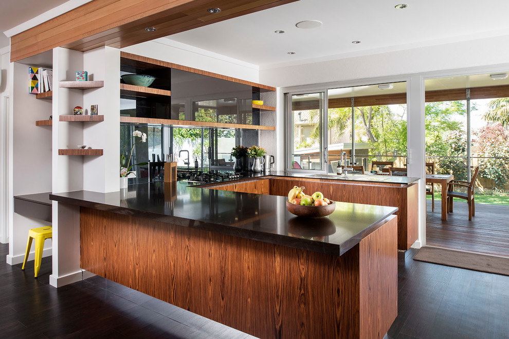 Immagine di una cucina ad U minimal con ante lisce, ante in legno scuro, paraspruzzi nero e paraspruzzi con lastra di vetro