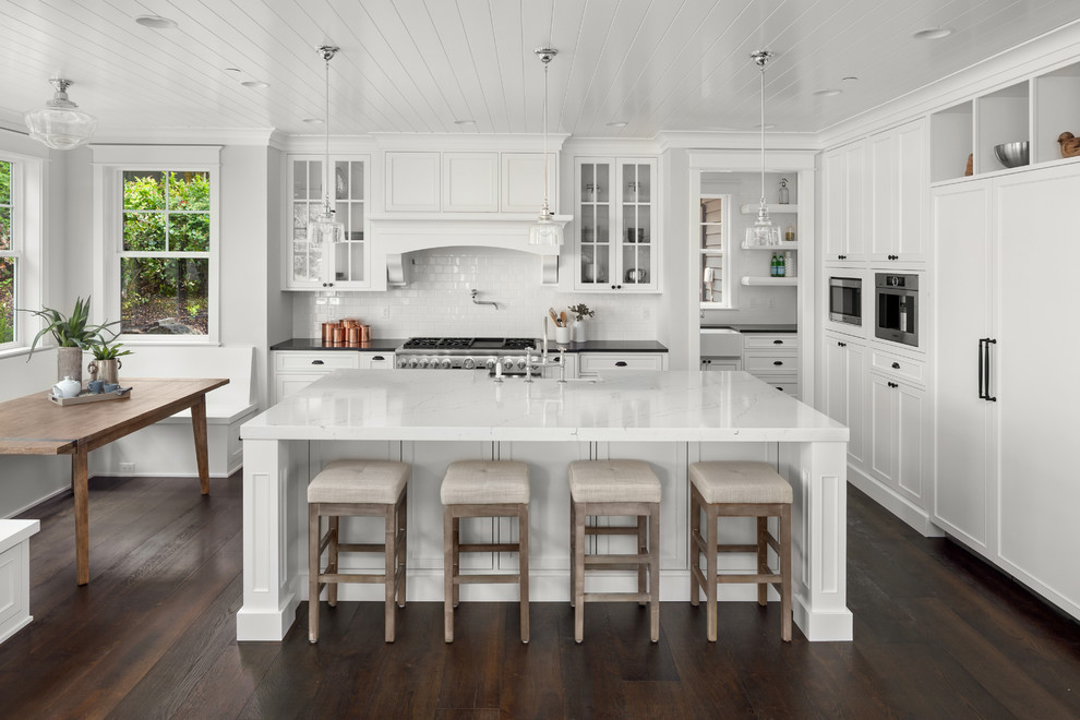 Design ideas for a classic l-shaped kitchen/diner in Other with a belfast sink, white cabinets, engineered stone countertops, white splashback, porcelain splashback, white worktops, beaded cabinets, integrated appliances, dark hardwood flooring, an island and brown floors.