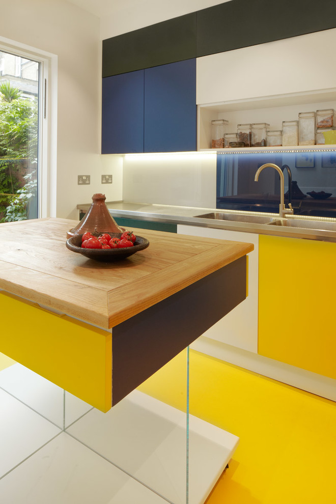 Modern inredning av ett mellanstort kök, med en enkel diskho, släta luckor, bänkskiva i rostfritt stål, gult stänkskydd, glaspanel som stänkskydd, rostfria vitvaror, linoleumgolv och en köksö