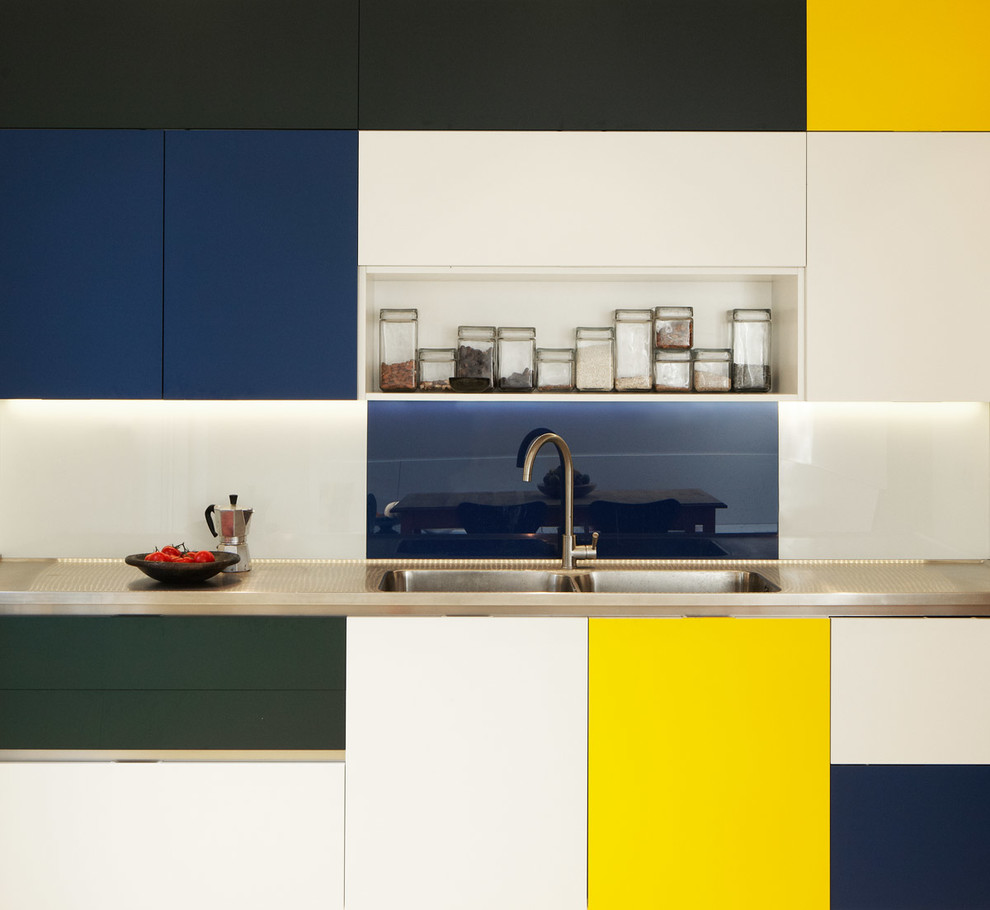 Design ideas for a medium sized contemporary u-shaped open plan kitchen in London with a single-bowl sink, flat-panel cabinets, stainless steel worktops, yellow splashback, glass sheet splashback, stainless steel appliances, lino flooring and an island.
