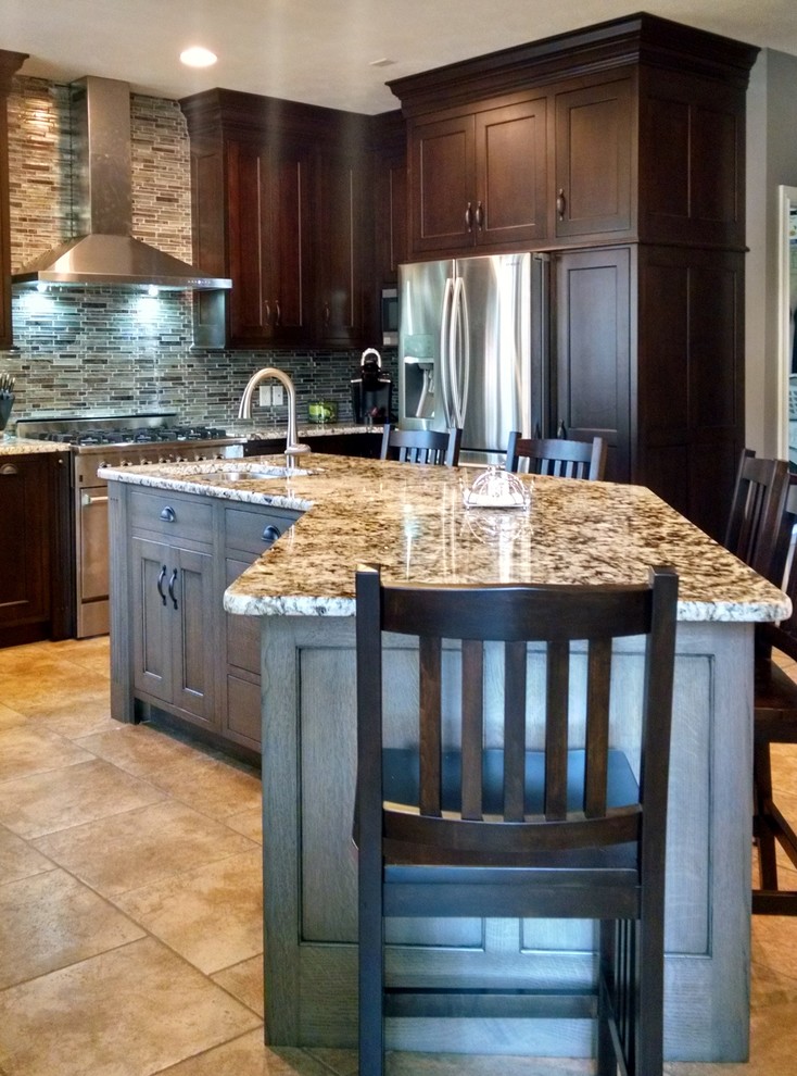 This is an example of a large traditional u-shaped open plan kitchen in Detroit with a submerged sink, flat-panel cabinets, dark wood cabinets, glass tiled splashback, stainless steel appliances, travertine flooring and an island.
