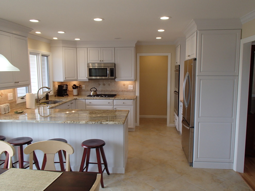 Bild på ett mellanstort funkis kök, med en nedsänkt diskho, luckor med upphöjd panel, vita skåp, granitbänkskiva, beige stänkskydd, stänkskydd i keramik, rostfria vitvaror, klinkergolv i porslin, en halv köksö och beiget golv