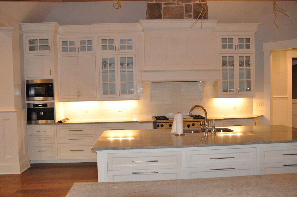 Idéer för att renovera ett stort vintage vit vitt kök, med en undermonterad diskho, luckor med infälld panel, vita skåp, marmorbänkskiva, vitt stänkskydd, stänkskydd i tunnelbanekakel, rostfria vitvaror, mellanmörkt trägolv, flera köksöar och brunt golv