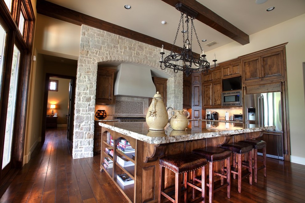 Eat-in kitchen - mid-sized traditional l-shaped medium tone wood floor eat-in kitchen idea in Austin with an undermount sink, raised-panel cabinets, medium tone wood cabinets, onyx countertops, beige backsplash, stone tile backsplash, stainless steel appliances and an island