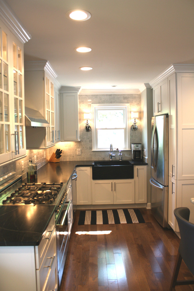 Example of a mid-sized beach style u-shaped dark wood floor eat-in kitchen design in Charlotte with a farmhouse sink, shaker cabinets, white cabinets, soapstone countertops, white backsplash, subway tile backsplash, stainless steel appliances and a peninsula