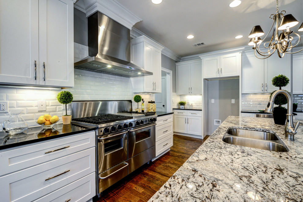 This is an example of a large traditional l-shaped open plan kitchen in Atlanta with a double-bowl sink, flat-panel cabinets, white cabinets, granite worktops, white splashback, metro tiled splashback, stainless steel appliances, medium hardwood flooring and an island.