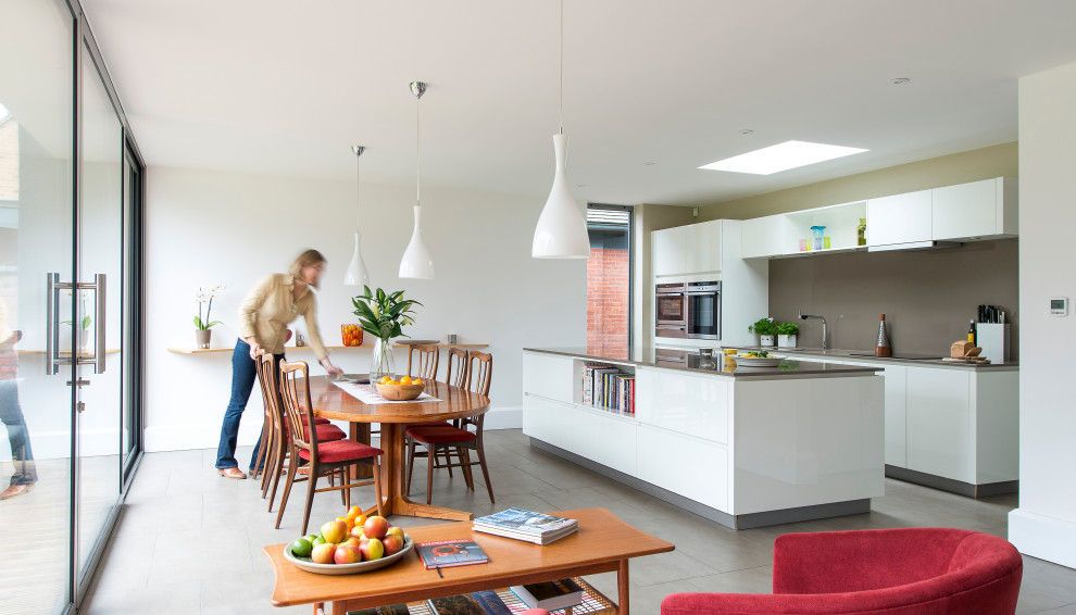 This is an example of a medium sized contemporary galley kitchen/diner in Other with a submerged sink, flat-panel cabinets, white cabinets, grey splashback, integrated appliances, an island, grey floors and grey worktops.