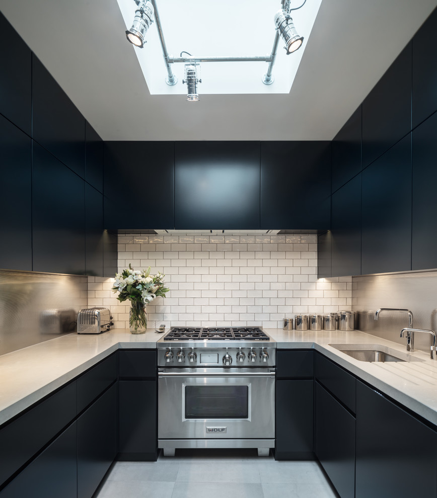 This is an example of a small modern u-shaped kitchen in London with a submerged sink, flat-panel cabinets, blue cabinets, quartz worktops, white splashback, metro tiled splashback and grey floors.