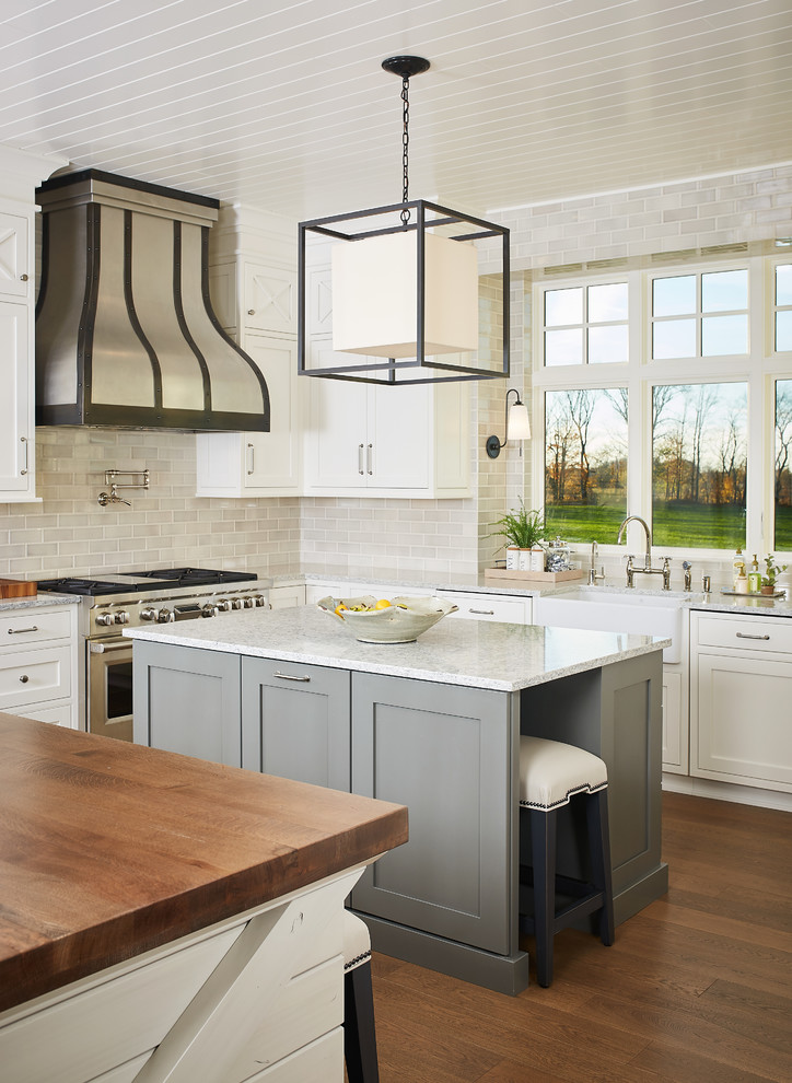 Large farmhouse u-shaped medium tone wood floor and brown floor eat-in kitchen photo in Grand Rapids with a farmhouse sink, recessed-panel cabinets, white cabinets, quartz countertops, multicolored backsplash, ceramic backsplash, stainless steel appliances and two islands