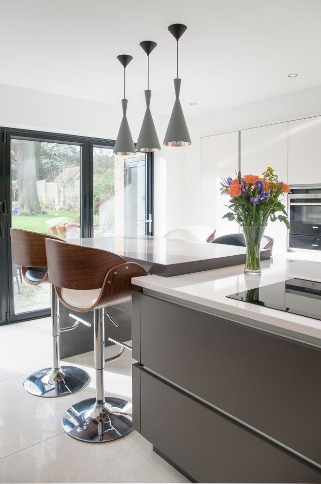 Design ideas for a large modern galley open plan kitchen in Kent with a built-in sink, flat-panel cabinets, white cabinets, glass worktops, beige splashback, glass tiled splashback, stainless steel appliances, slate flooring, a breakfast bar and beige floors.