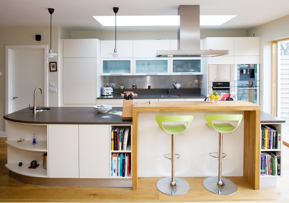 Foto på ett mellanstort funkis parallellkök, med en undermonterad diskho, släta luckor, vita skåp, stänkskydd med metallisk yta, ljust trägolv och en köksö