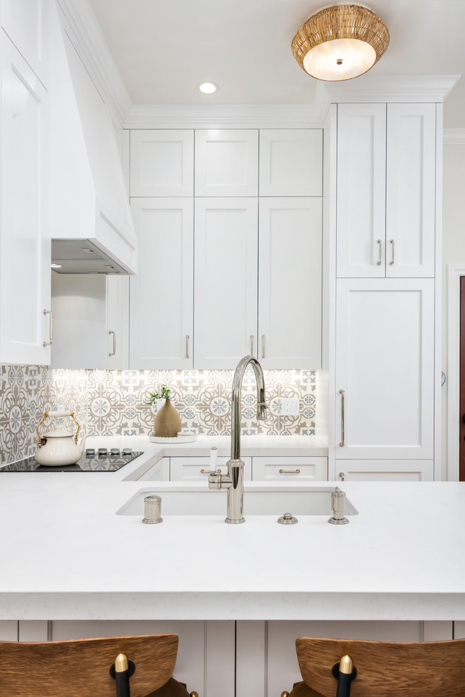 Inredning av ett lantligt litet vit vitt kök, med en undermonterad diskho, luckor med upphöjd panel, vita skåp, bänkskiva i kvarts, flerfärgad stänkskydd, stänkskydd i keramik, integrerade vitvaror, mellanmörkt trägolv, en halv köksö och brunt golv
