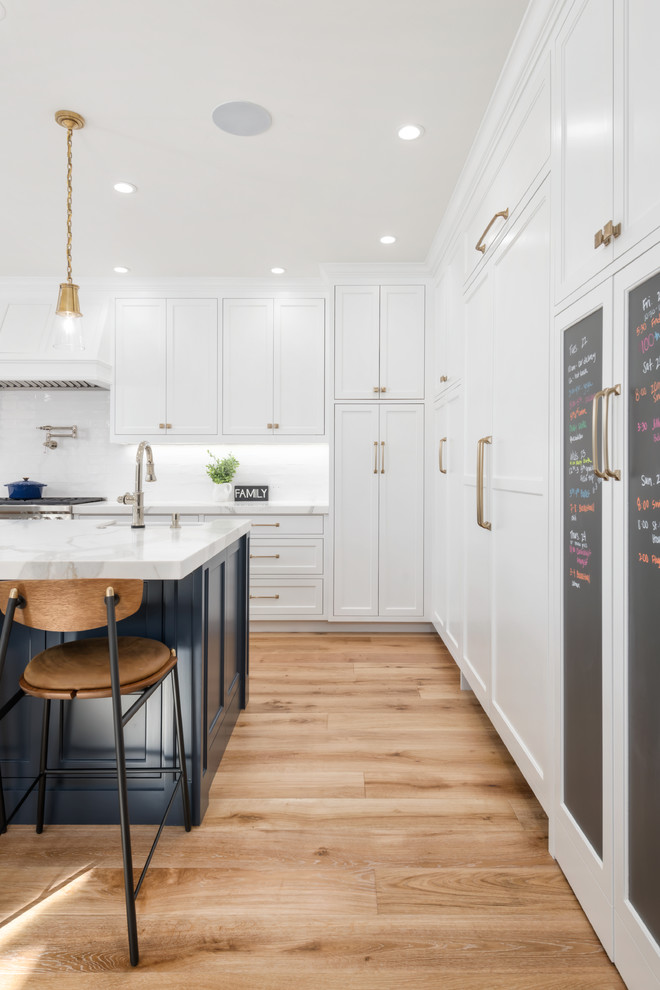 Example of a large cottage u-shaped medium tone wood floor and brown floor open concept kitchen design in San Francisco with a farmhouse sink, beaded inset cabinets, white cabinets, marble countertops, white backsplash, ceramic backsplash, paneled appliances, an island and white countertops