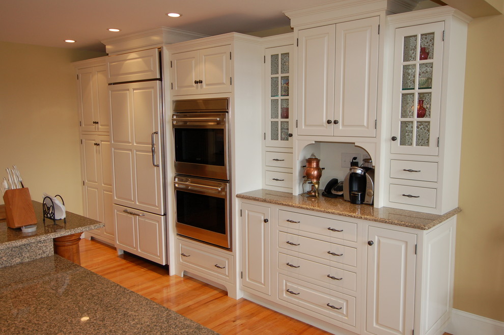 Klassisk inredning av ett stort kök, med en undermonterad diskho, luckor med upphöjd panel, vita skåp, granitbänkskiva, beige stänkskydd, stänkskydd i keramik, integrerade vitvaror, mellanmörkt trägolv och en köksö