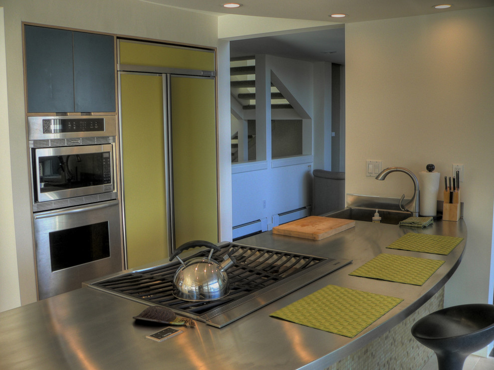 Moderne Küche mit flächenbündigen Schrankfronten, grünen Schränken, Edelstahl-Arbeitsplatte und Elektrogeräten mit Frontblende in Denver
