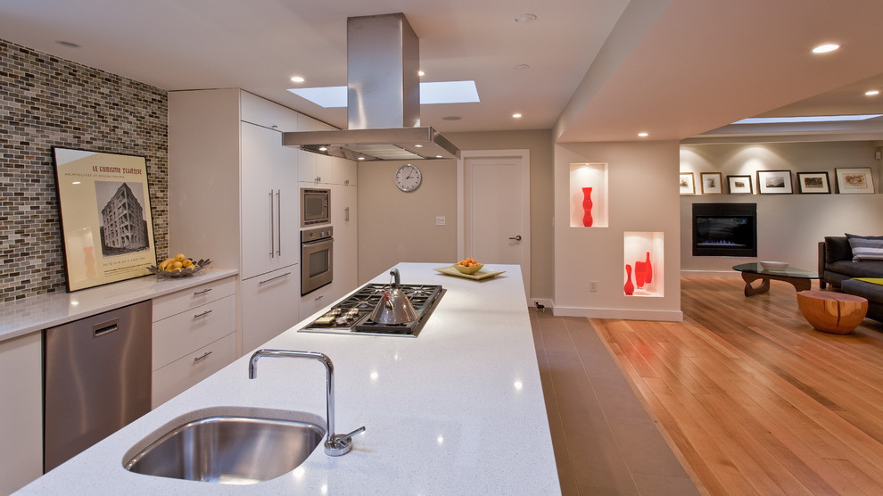 Bild på ett funkis kök med öppen planlösning, med rostfria vitvaror, en undermonterad diskho, släta luckor, vita skåp, flerfärgad stänkskydd och stänkskydd i mosaik