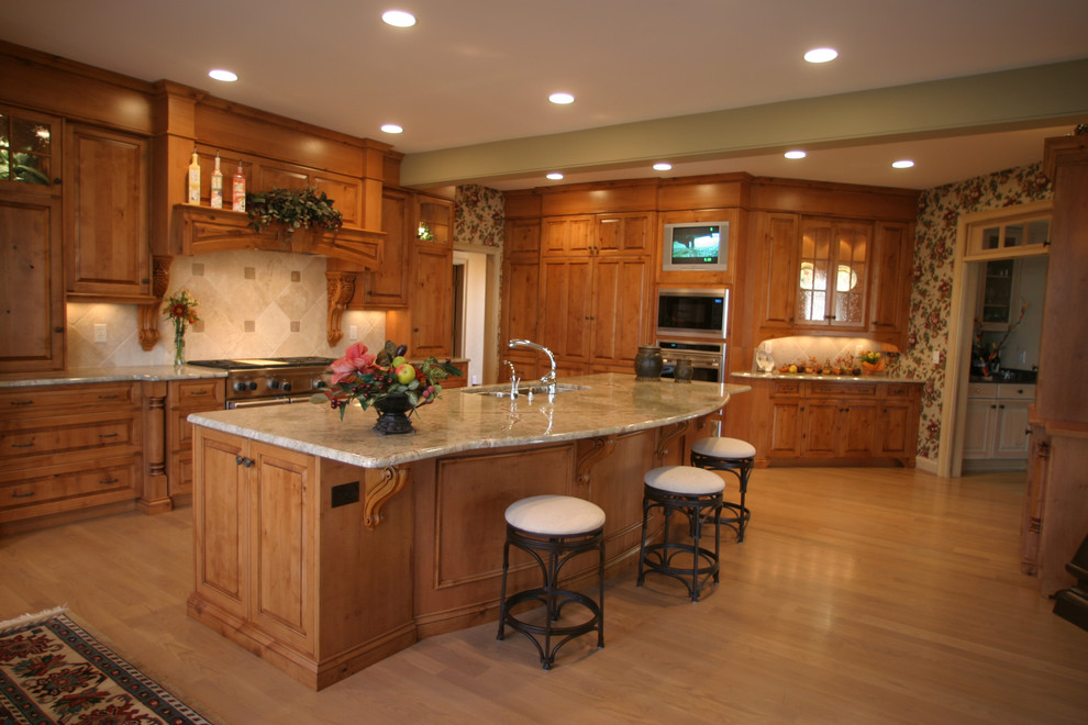 Klassisk inredning av ett stort kök, med en dubbel diskho, luckor med upphöjd panel, skåp i mellenmörkt trä, bänkskiva i täljsten, beige stänkskydd, stänkskydd i travertin, rostfria vitvaror, ljust trägolv, en köksö och beiget golv