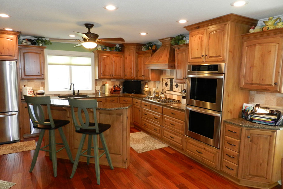 Example of a mid-sized classic l-shaped medium tone wood floor eat-in kitchen design in Cleveland with an undermount sink, raised-panel cabinets, light wood cabinets, granite countertops, beige backsplash, porcelain backsplash, stainless steel appliances and an island
