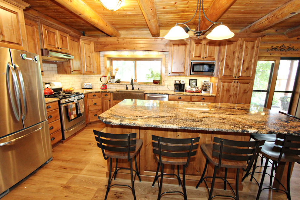 Inredning av ett rustikt mellanstort brun brunt kök, med en rustik diskho, luckor med upphöjd panel, skåp i mellenmörkt trä, granitbänkskiva, beige stänkskydd, stänkskydd i stenkakel, rostfria vitvaror, ljust trägolv och en köksö