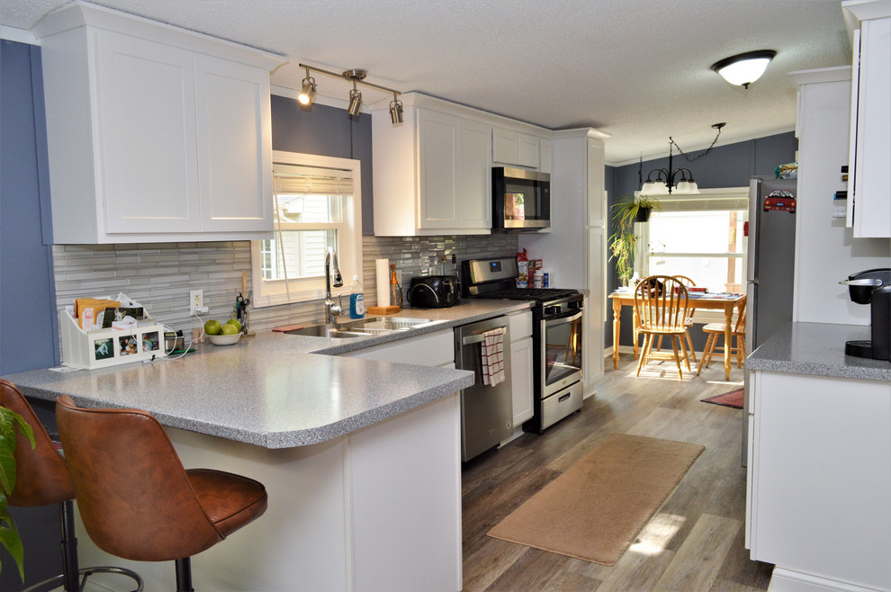 Klassisk inredning av ett mellanstort grå grått kök, med en undermonterad diskho, skåp i shakerstil, vita skåp, laminatbänkskiva, grått stänkskydd, stänkskydd i stickkakel, rostfria vitvaror, laminatgolv, en halv köksö och brunt golv