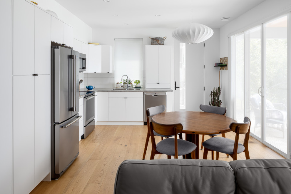 Eat-in kitchen - mid-sized contemporary l-shaped medium tone wood floor and brown floor eat-in kitchen idea in Other with a drop-in sink, flat-panel cabinets, white cabinets, quartz countertops, white backsplash, subway tile backsplash, stainless steel appliances, no island and gray countertops