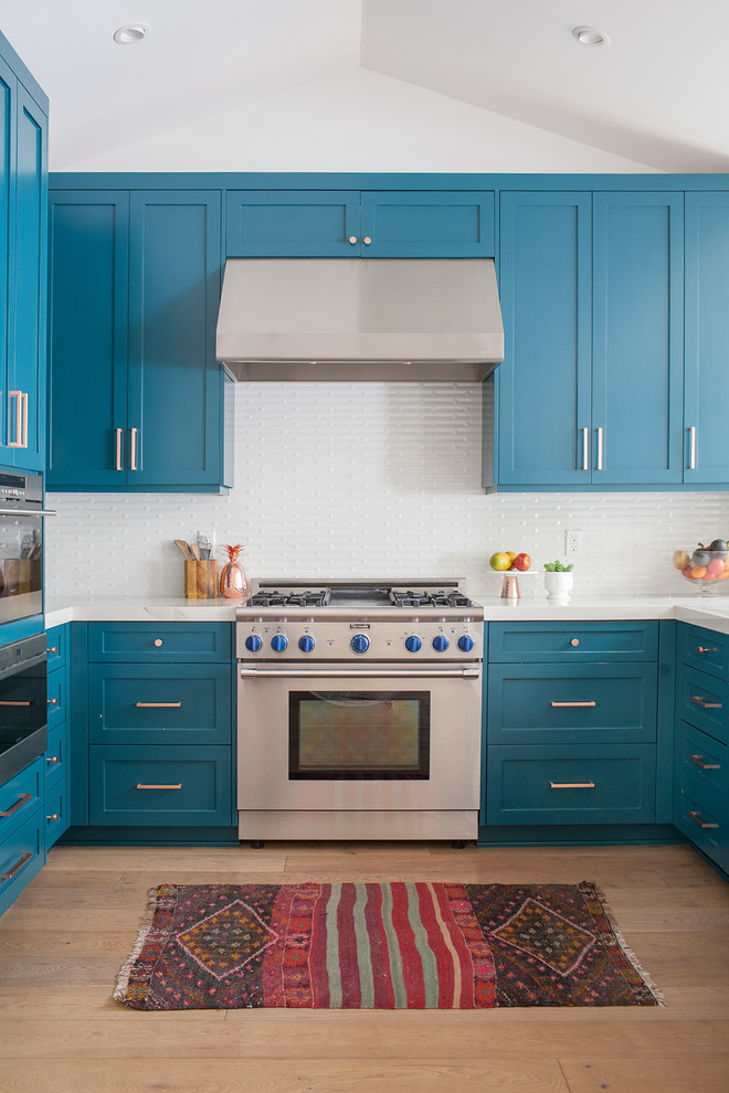 オレンジカウンティにある高級なトランジショナルスタイルのおしゃれなキッチン (シェーカースタイル扉のキャビネット、青いキャビネット、白いキッチンパネル、シルバーの調理設備、淡色無垢フローリング、ベージュの床、アイランドなし) の写真