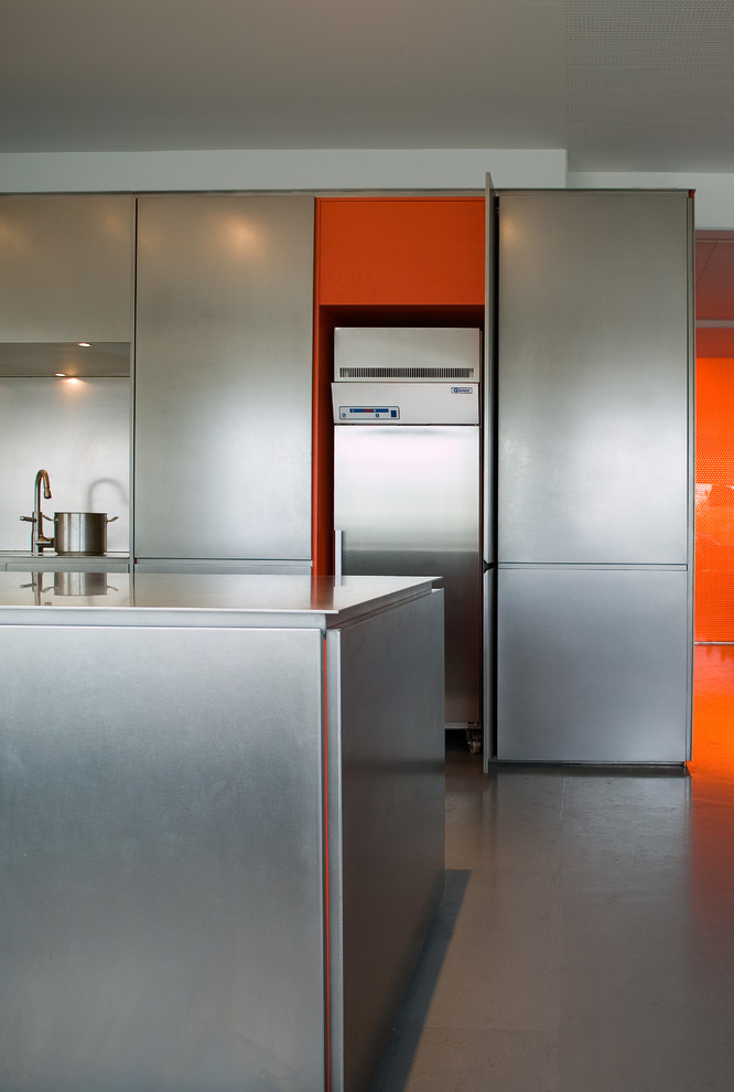 Exempel på ett industriellt kök, med släta luckor, skåp i rostfritt stål, bänkskiva i rostfritt stål, vitt stänkskydd, betonggolv och en köksö