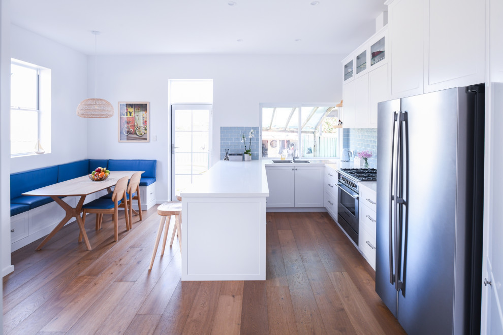 シドニーにある広いモダンスタイルのおしゃれなキッチン (ドロップインシンク、シェーカースタイル扉のキャビネット、白いキャビネット、クオーツストーンカウンター、青いキッチンパネル、サブウェイタイルのキッチンパネル、シルバーの調理設備、濃色無垢フローリング、茶色い床、白いキッチンカウンター) の写真