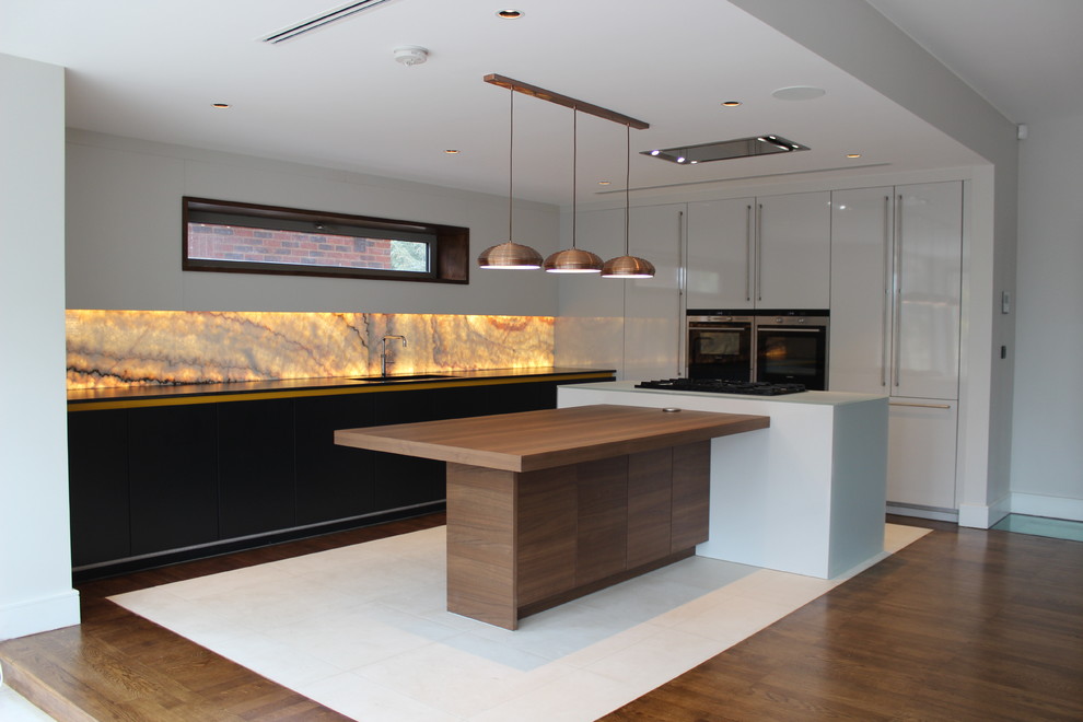ロンドンにある高級な中くらいなコンテンポラリースタイルのおしゃれなキッチン (一体型シンク、フラットパネル扉のキャビネット、オレンジのキッチンパネル、ガラス板のキッチンパネル、黒い調理設備) の写真