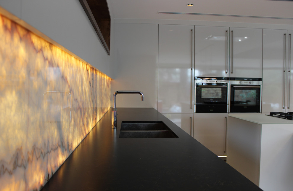 Источник вдохновения для домашнего уюта: угловая кухня среднего размера в современном стиле с обеденным столом, монолитной мойкой, плоскими фасадами, оранжевым фартуком, фартуком из стекла, черной техникой и островом