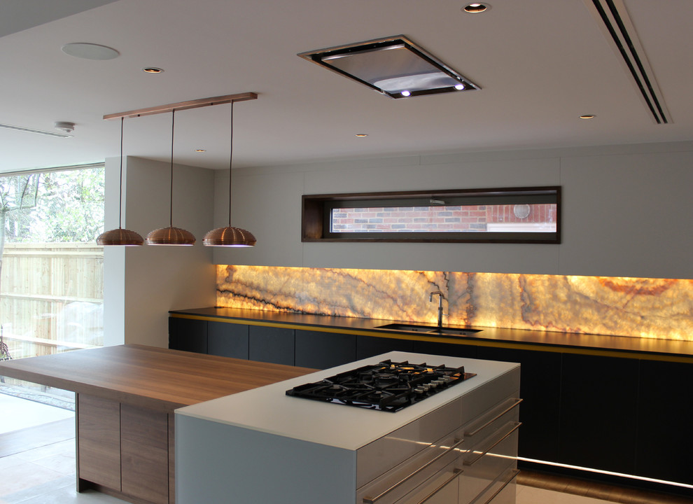 Mittelgroße Moderne Wohnküche in L-Form mit integriertem Waschbecken, flächenbündigen Schrankfronten, Küchenrückwand in Orange, Glasrückwand, schwarzen Elektrogeräten und Kücheninsel in London