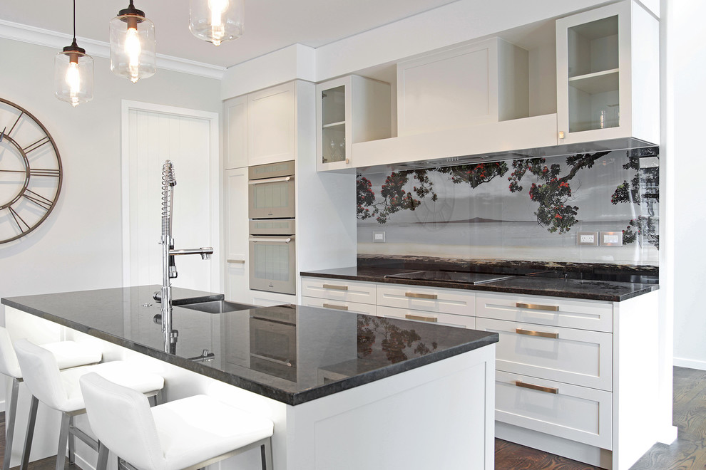 Einzeilige, Mittelgroße Moderne Wohnküche mit Waschbecken, weißen Schränken, Granit-Arbeitsplatte, Küchenrückwand in Schwarz, Glasrückwand, Küchengeräten aus Edelstahl, braunem Holzboden und Kücheninsel in Auckland