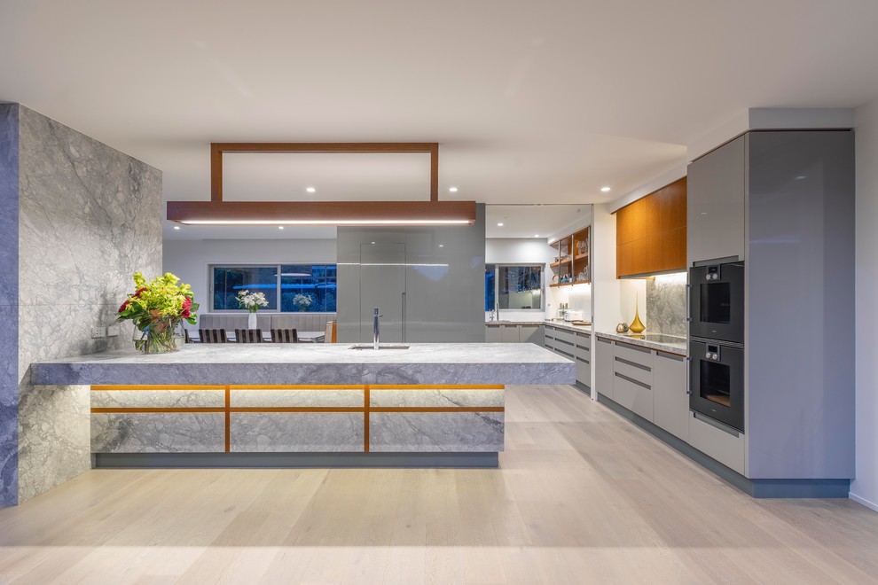 Foto på ett mycket stort funkis grå kök, med en undermonterad diskho, släta luckor, grå skåp, granitbänkskiva, ljust trägolv, beiget golv, grått stänkskydd, integrerade vitvaror och en halv köksö