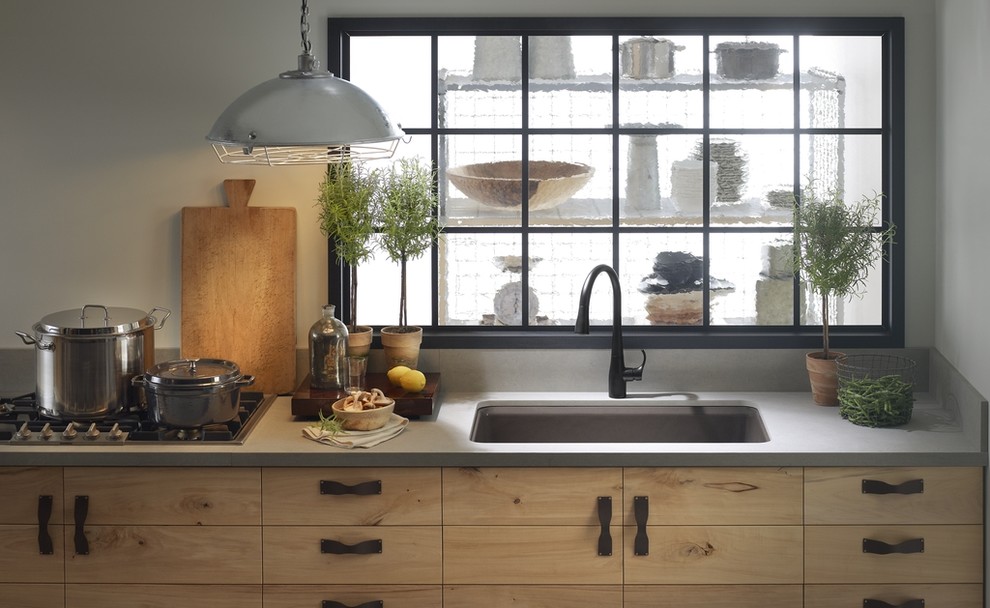 Cette photo montre une cuisine linéaire éclectique en bois clair fermée avec un évier encastré, un placard à porte plane, un plan de travail en quartz et un électroménager en acier inoxydable.