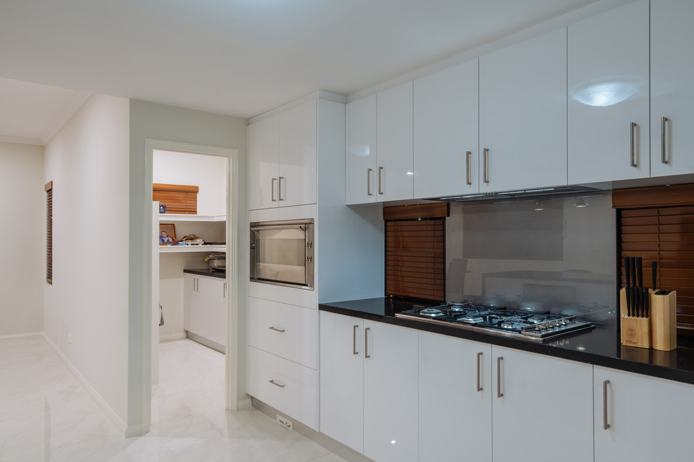 Imagen de cocina contemporánea grande abierta con puertas de armario blancas, salpicadero verde, electrodomésticos de acero inoxidable y una isla