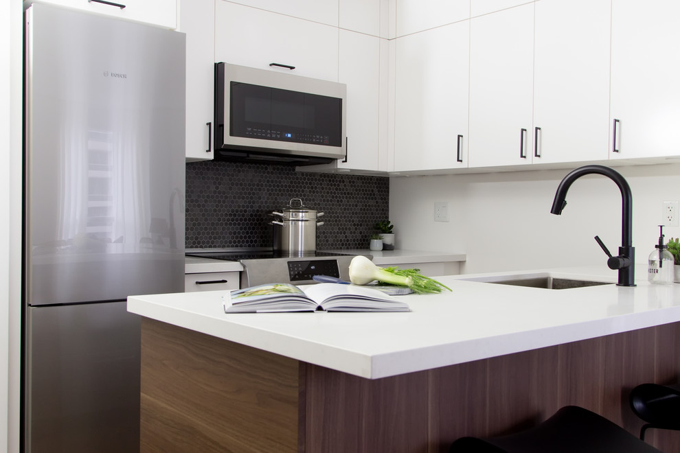 Imagen de cocina comedor actual pequeña con fregadero de un seno, armarios con paneles lisos, puertas de armario blancas, encimera de cuarzo compacto, salpicadero negro, salpicadero con mosaicos de azulejos, electrodomésticos negros, suelo de madera en tonos medios, península y encimeras blancas