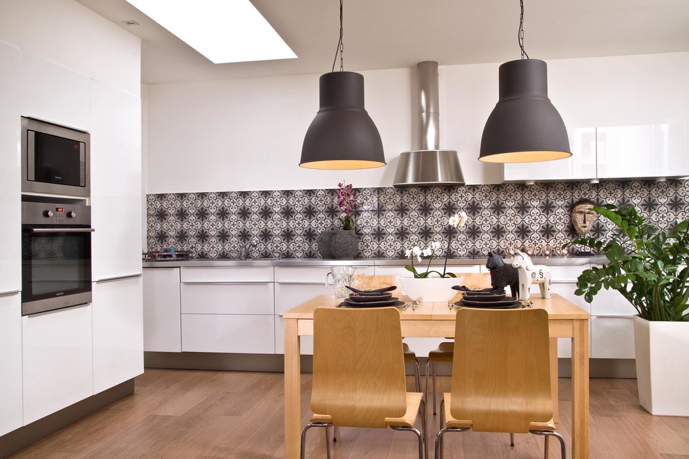 Example of a trendy eat-in kitchen design in Other with flat-panel cabinets, stainless steel appliances, white cabinets, stainless steel countertops and black backsplash