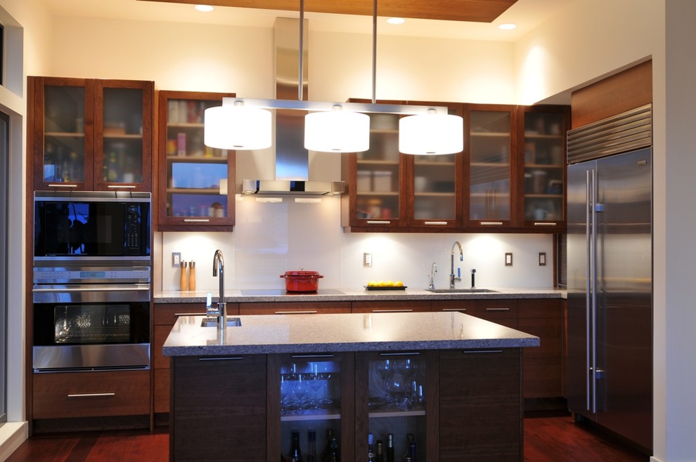Modern inredning av ett litet linjärt kök med öppen planlösning, med en undermonterad diskho, släta luckor, skåp i mellenmörkt trä, bänkskiva i kvarts, vitt stänkskydd, glaspanel som stänkskydd, rostfria vitvaror och mellanmörkt trägolv