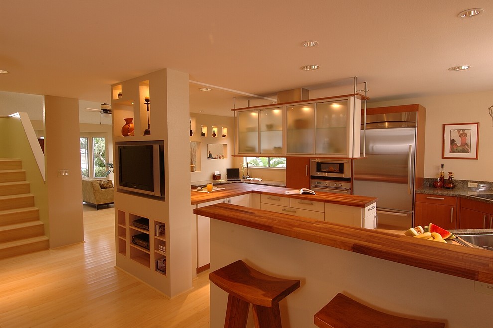 На фото: кухня-гостиная в восточном стиле с стеклянными фасадами, техникой из нержавеющей стали, деревянной столешницей и барной стойкой с