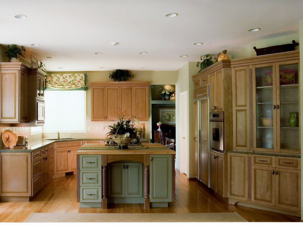 Kitchen - mid-sized traditional u-shaped medium tone wood floor and brown floor kitchen idea in Seattle with an undermount sink, raised-panel cabinets, white backsplash, ceramic backsplash, paneled appliances, an island, medium tone wood cabinets, granite countertops and green countertops