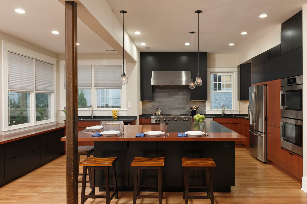 ワシントンD.C.にあるコンテンポラリースタイルのおしゃれなキッチン (フラットパネル扉のキャビネット、黒いキャビネット、木材カウンター、グレーのキッチンパネル、シルバーの調理設備、無垢フローリング、茶色い床) の写真