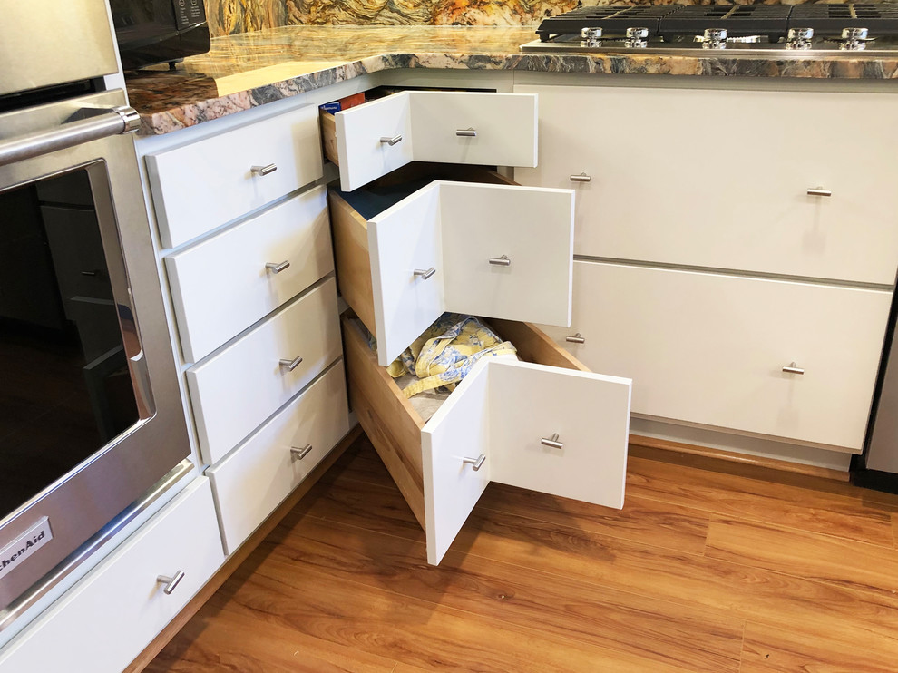 Photo of a medium sized contemporary u-shaped kitchen/diner in Baltimore with a submerged sink, flat-panel cabinets, white cabinets, granite worktops, stainless steel appliances, laminate floors, an island, brown floors and multicoloured worktops.