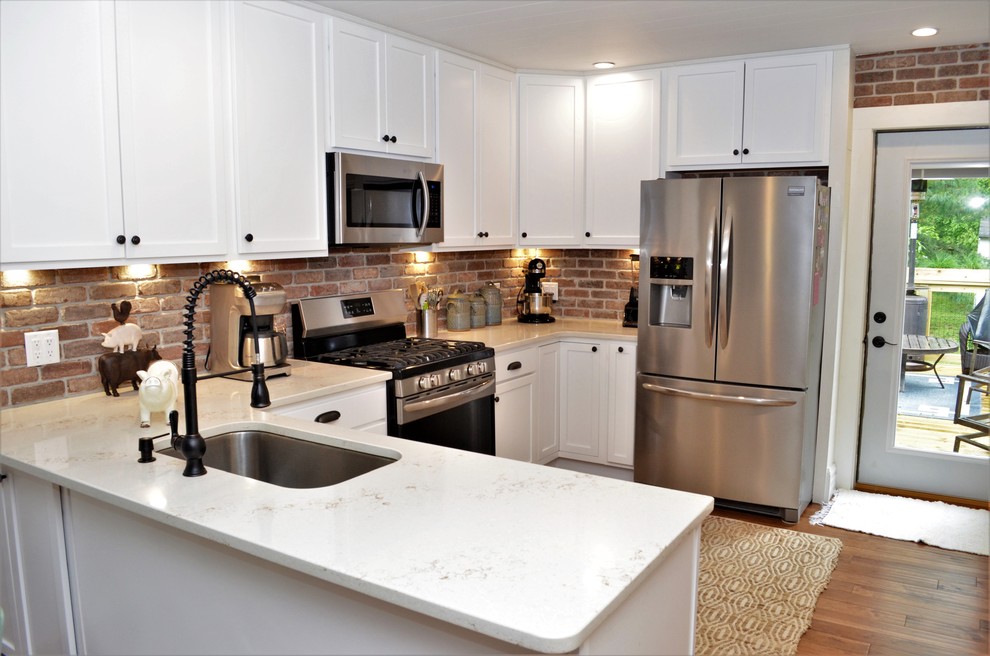 Foto på ett mellanstort lantligt vit kök, med en undermonterad diskho, skåp i shakerstil, vita skåp, bänkskiva i kvartsit, stänkskydd i tegel, brunt stänkskydd, rostfria vitvaror, mellanmörkt trägolv, brunt golv och en halv köksö