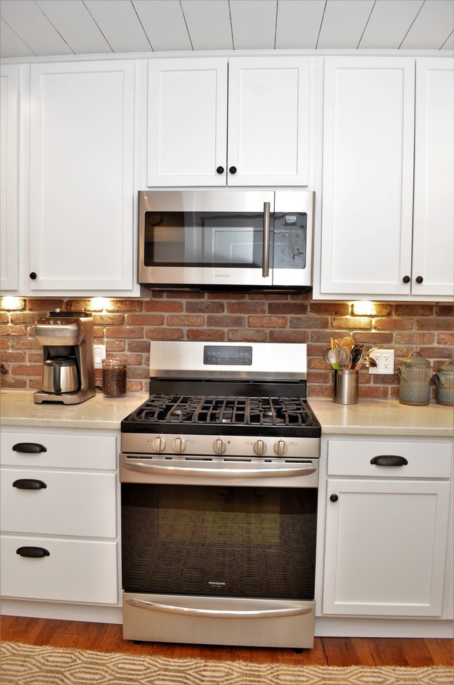 Inredning av ett lantligt mellanstort vit vitt kök, med skåp i shakerstil, vita skåp, bänkskiva i kvartsit, stänkskydd i tegel, en undermonterad diskho, brunt stänkskydd, rostfria vitvaror, mellanmörkt trägolv och brunt golv