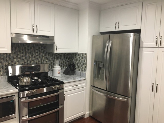 Modern inredning av ett mellanstort kök, med en undermonterad diskho, luckor med upphöjd panel, vita skåp, bänkskiva i kvarts, flerfärgad stänkskydd, glaspanel som stänkskydd, rostfria vitvaror, laminatgolv och en halv köksö