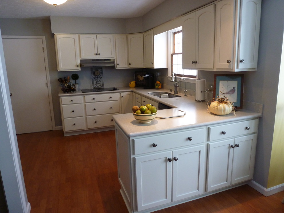 Example of a mid-sized classic galley light wood floor eat-in kitchen design in Chicago with an undermount sink, flat-panel cabinets, white cabinets, solid surface countertops, white backsplash, stainless steel appliances and a peninsula