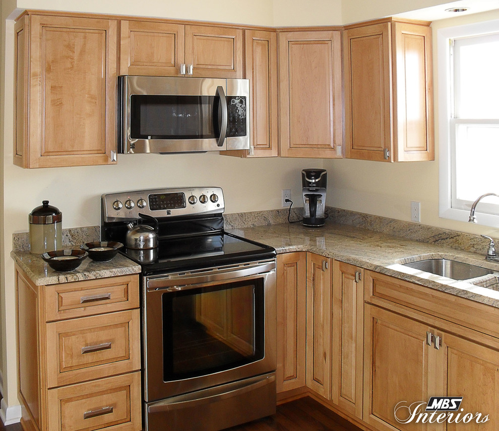 Exemple d'une cuisine américaine chic en U et bois clair avec un placard avec porte à panneau surélevé, un plan de travail en granite et un électroménager en acier inoxydable.